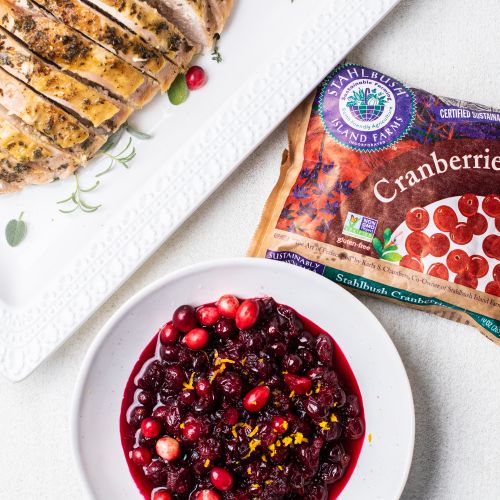 A dish of roasted turkey with a bag of Stahlbush cranberries and a bowl of cranberry sauce