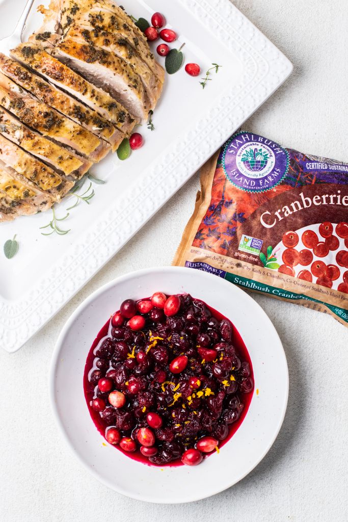 A dish of roasted turkey with a bag of Stahlbush cranberries and a bowl of cranberry sauce