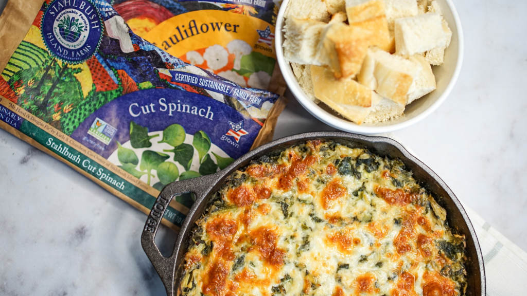 spinach artichoke dip in a cast iron with bags of frozen spinach