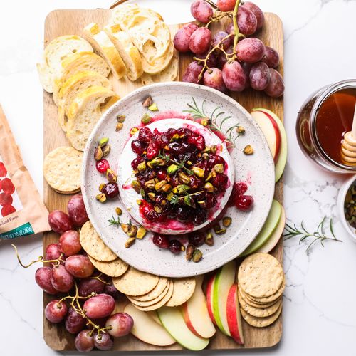 a charcuterie style spread on a wooden board with a baked brie with cranberry compote